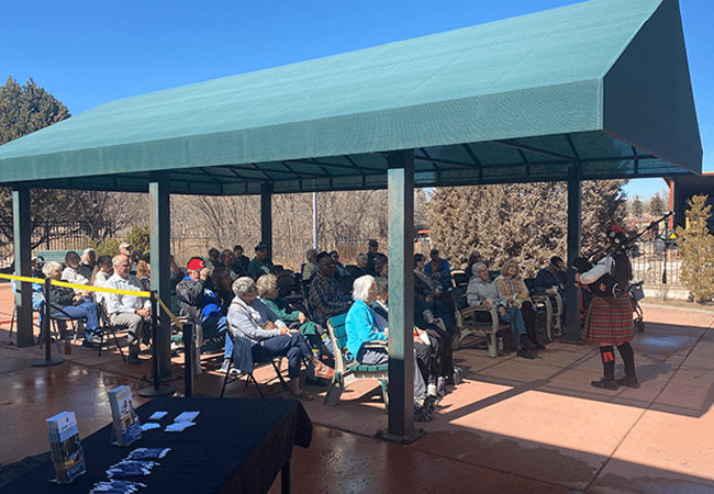 A group of senior citizens gathered under a pavilion for a bagpipe performance