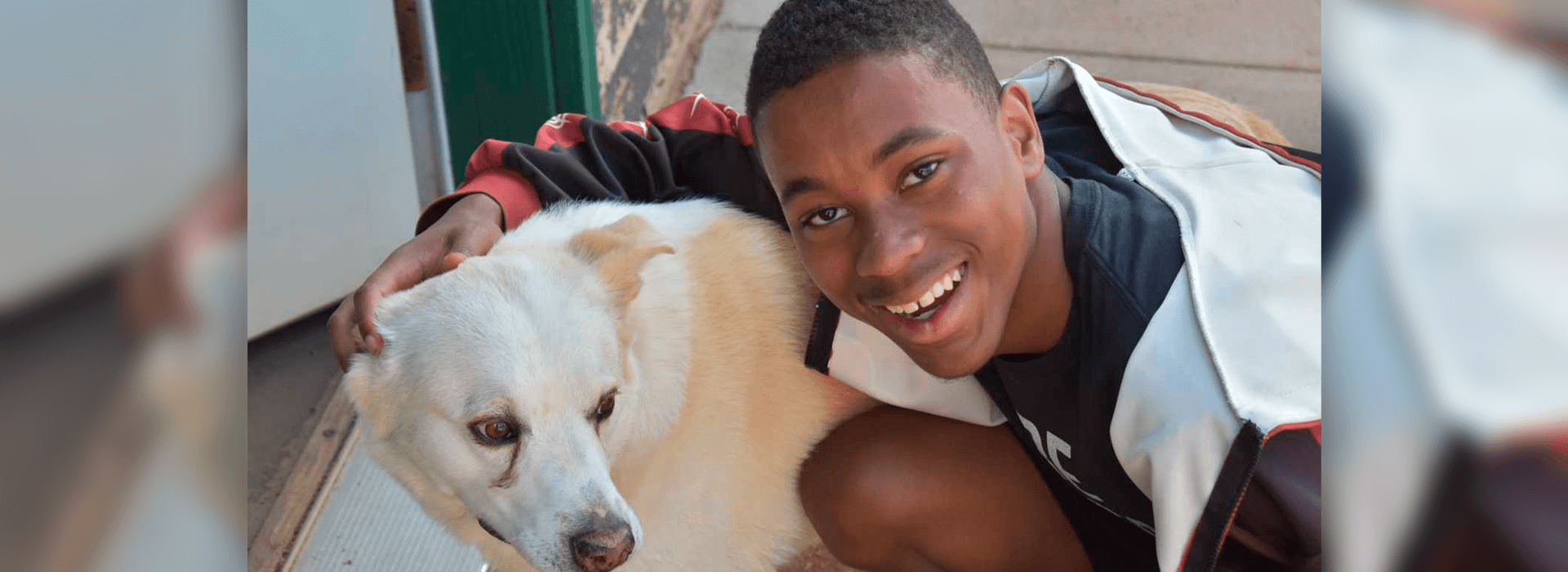 A boy smiling with his arm around a dog