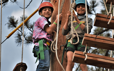 Two young boys smiling on top of a ropes course 