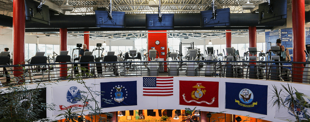The cardio equipment at the Southeast Armed Services YMCA gym with armed services flags hanging below